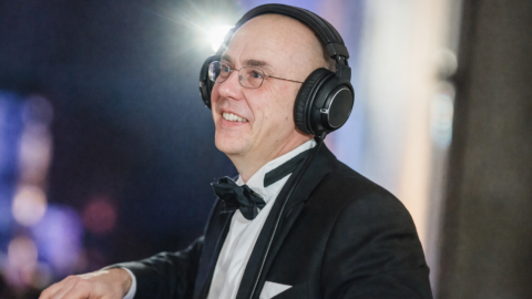 Dr. Frank in festlicher Kleidung mit Kopfhörern am DJ-Pult